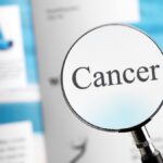 Kata “Cancer” terlihat jelas melalui kaca pembesar di atas majalah kesehatan.